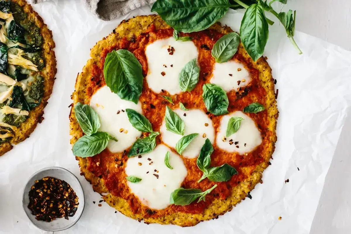 Pyszna pizza z kalafiora z pomidorami, mozzarellą i bazylią. Obok miseczka płatków chili.