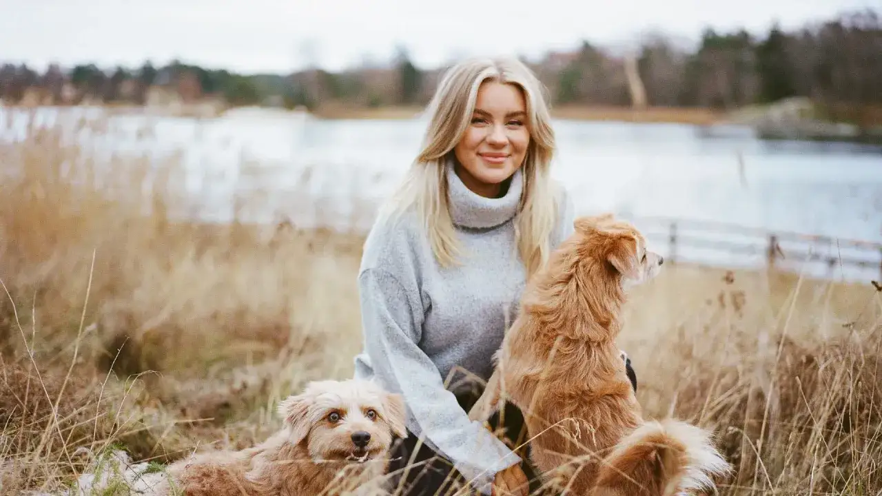 Therese Lindgren njuter av en höstdag vid vattnet med sina två hundar i ett torrt gräslandskap.