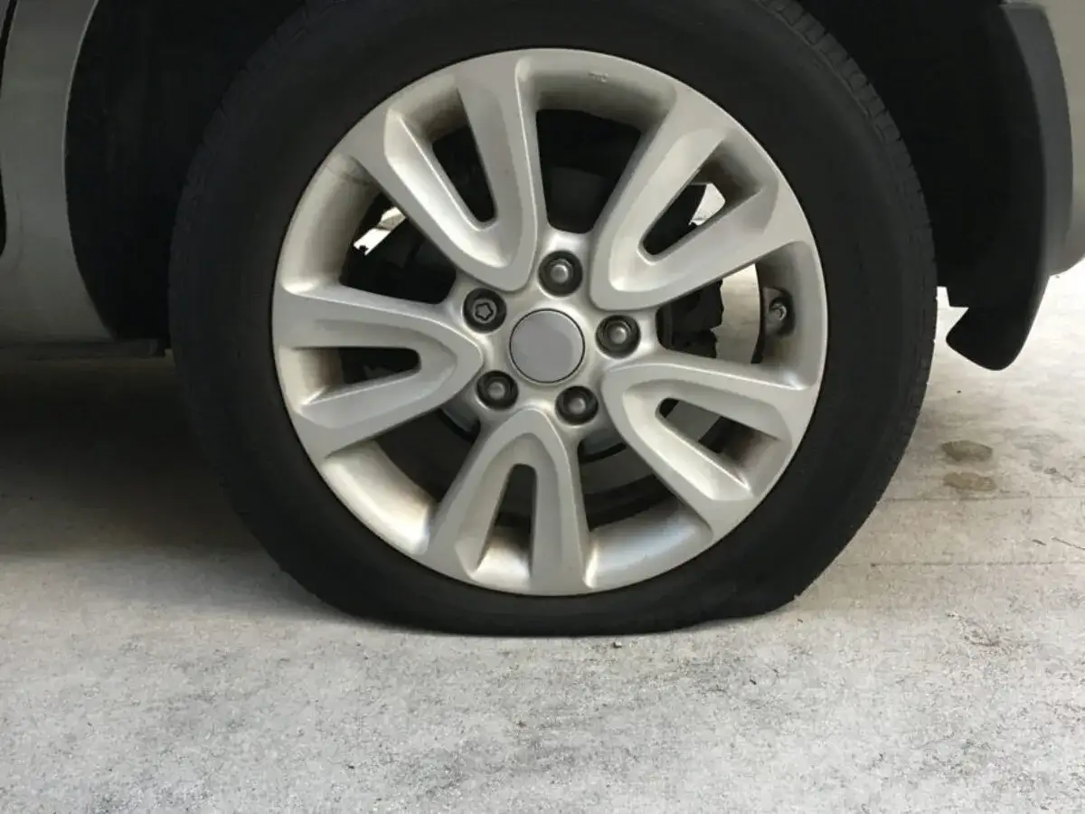 Roue de voiture avec une importante perte de pression pneu, le pneu est complètement à plat sur le sol.