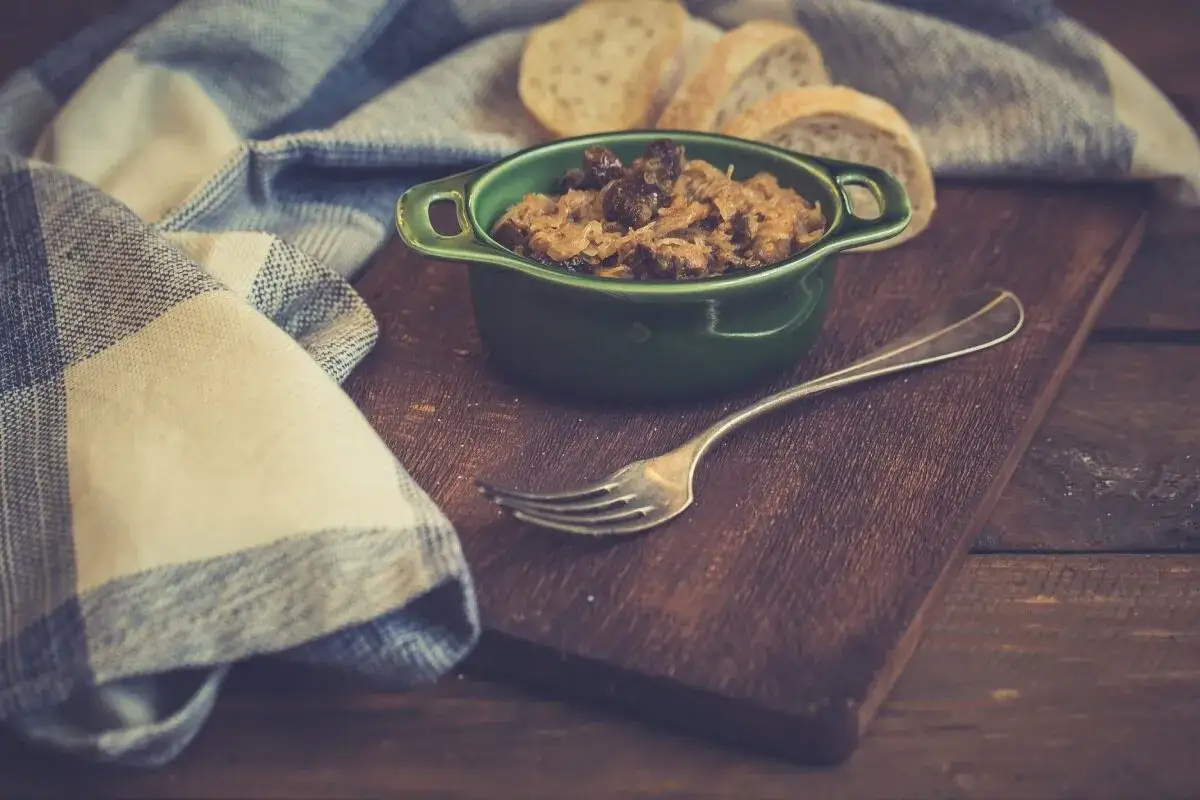 Pyszny bigos z szybkowaru w zielonej miseczce, obok kromki chleba i widelca. Idealny na chłodne dni.