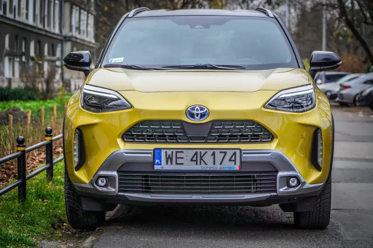 Żółta Toyota Yaris Cross, która hybryda pali najmniej, zaparkowana na tle kamienicy.
