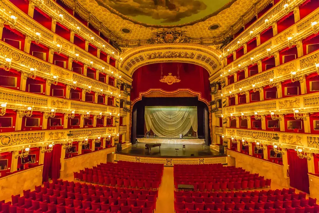 L'interno sontuoso di uno dei teatri più grandi d'Italia, con palchi dorati, velluto rosso e un palco pronto per uno spettacolo.