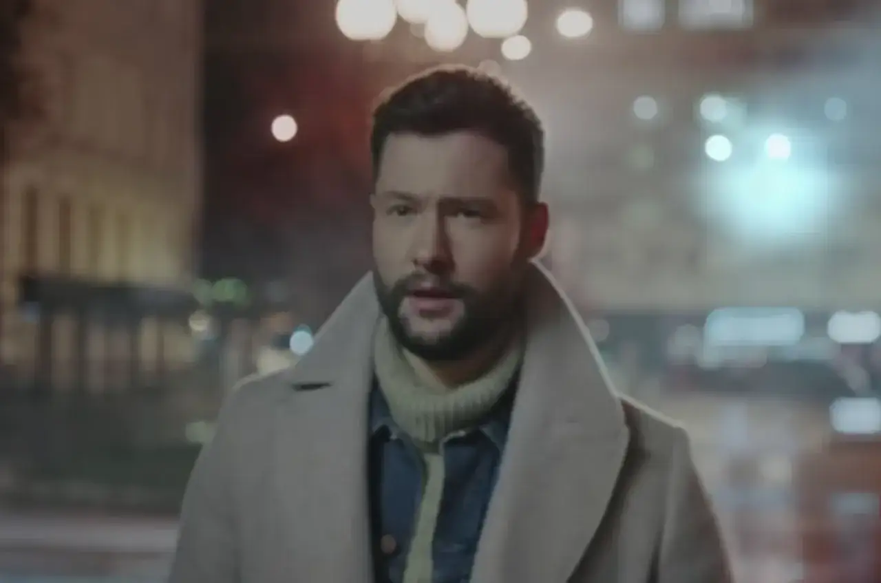 Calum Scott w płaszczu i golfie, w tle nocne miasto. Tekst