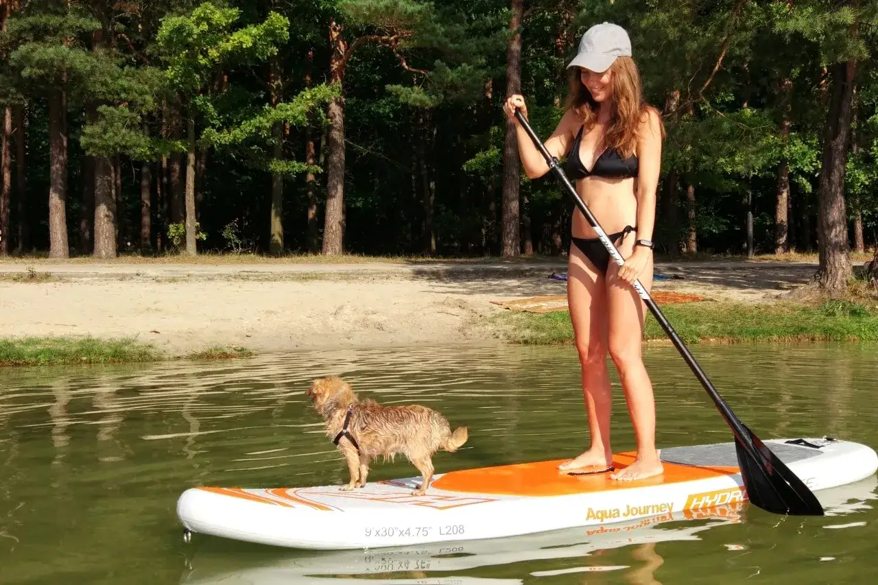 Dziewczyna na desce SUP z psem, ciesząca się słońcem i wodą. Sup co to? To świetna zabawa na jeziorze!
