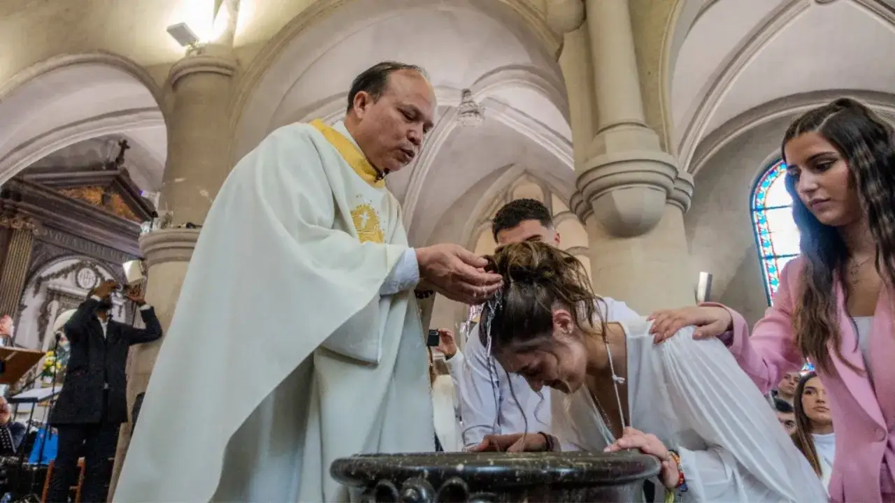 Kapłan polewa wodą głowę katechumenki podczas ceremonii chrztu w kościele.