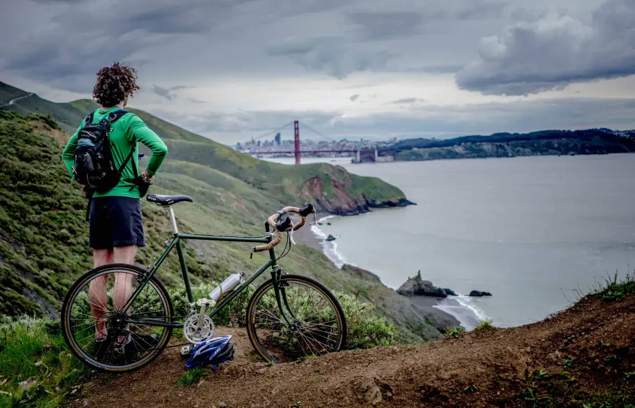 Wybierając się na rower przy 5 stopniach, postaw na warstwy: zielona bluza, ciemne spodenki i plecak to dobry start. Widok na most Golden Gate zachęca do jazdy.