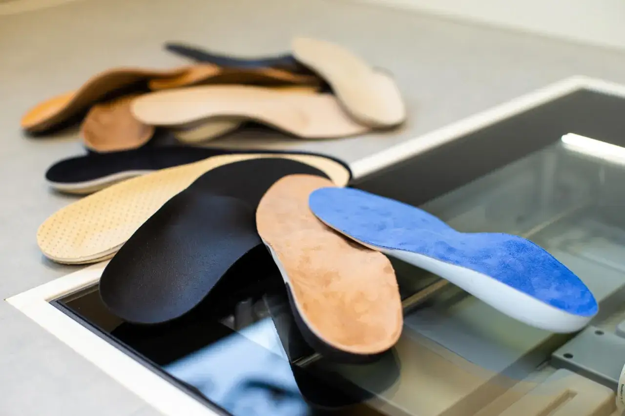 Verschiedene orthopädische Einlagen in Braun, Schwarz und Blau liegen auf einer Glasfläche. Informieren Sie sich über die orthopädische Einlagen Kostenübernahme.