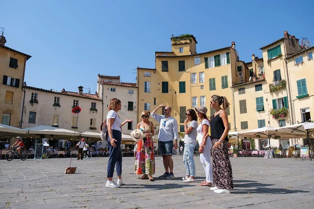 Un gruppo di persone ascolta una guida in una piazza di Lucca, godendosi un weekend di sole e cultura.