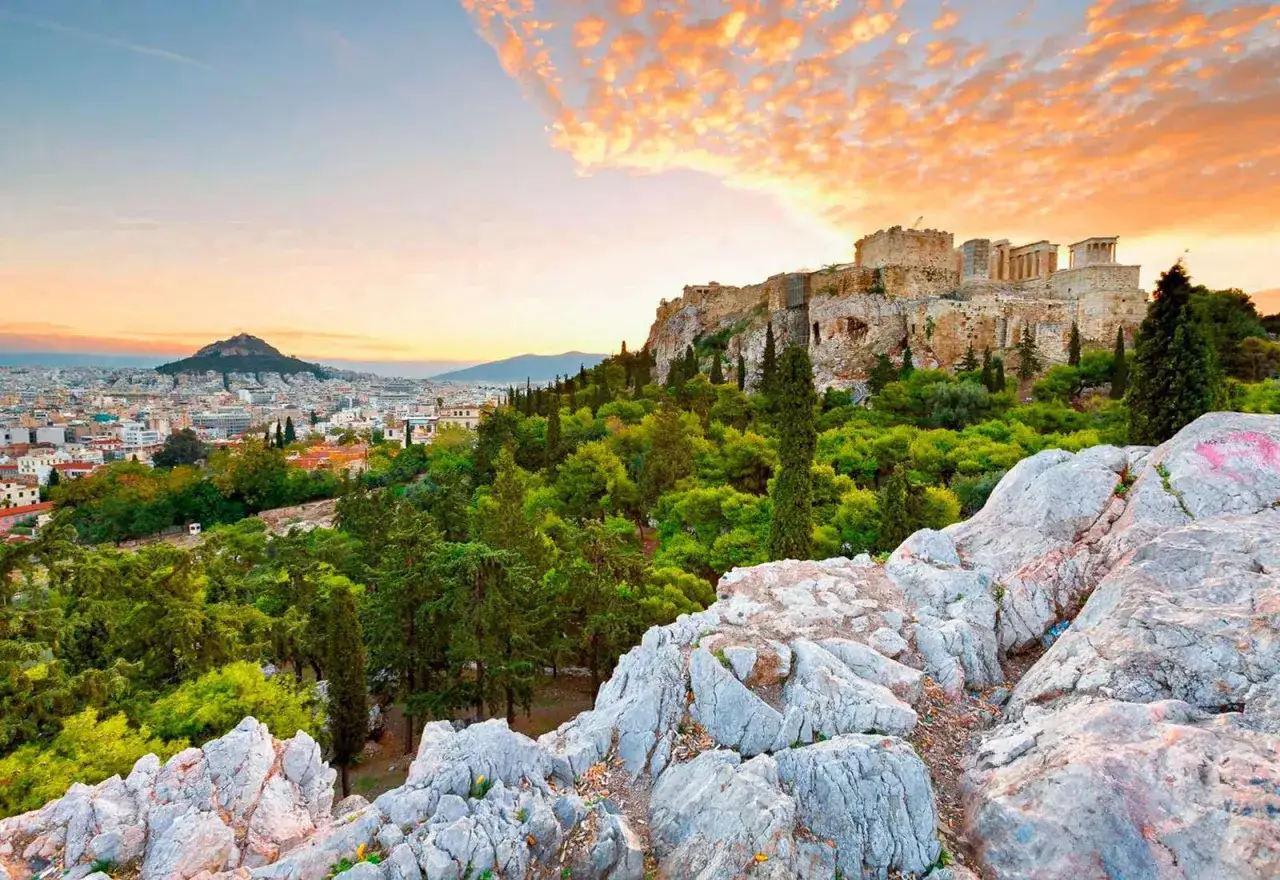Akropolis reser sig &ouml;ver Aten, greklands huvudstad, med en dramatisk solnedg&aring;ng i bakgrunden.