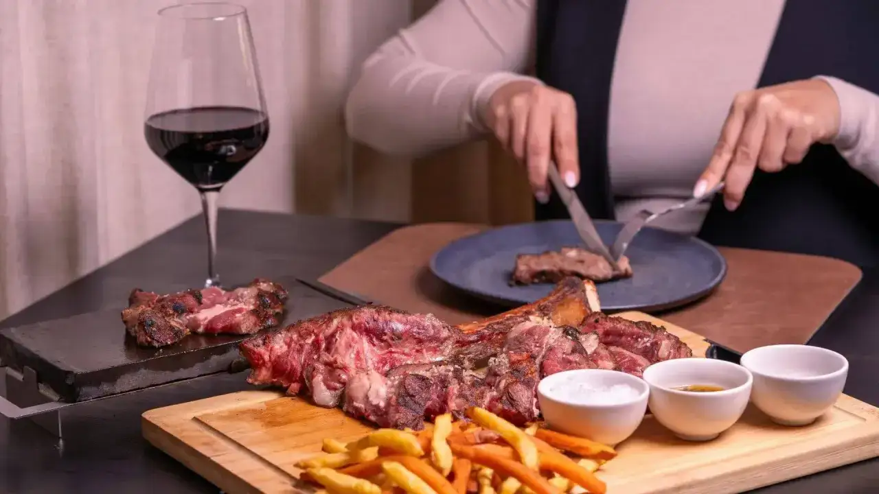 Idealne **jakie wino do wieprzowiny**? Czerwone wino i soczysta wieprzowina na desce, z frytkami i sosami.
