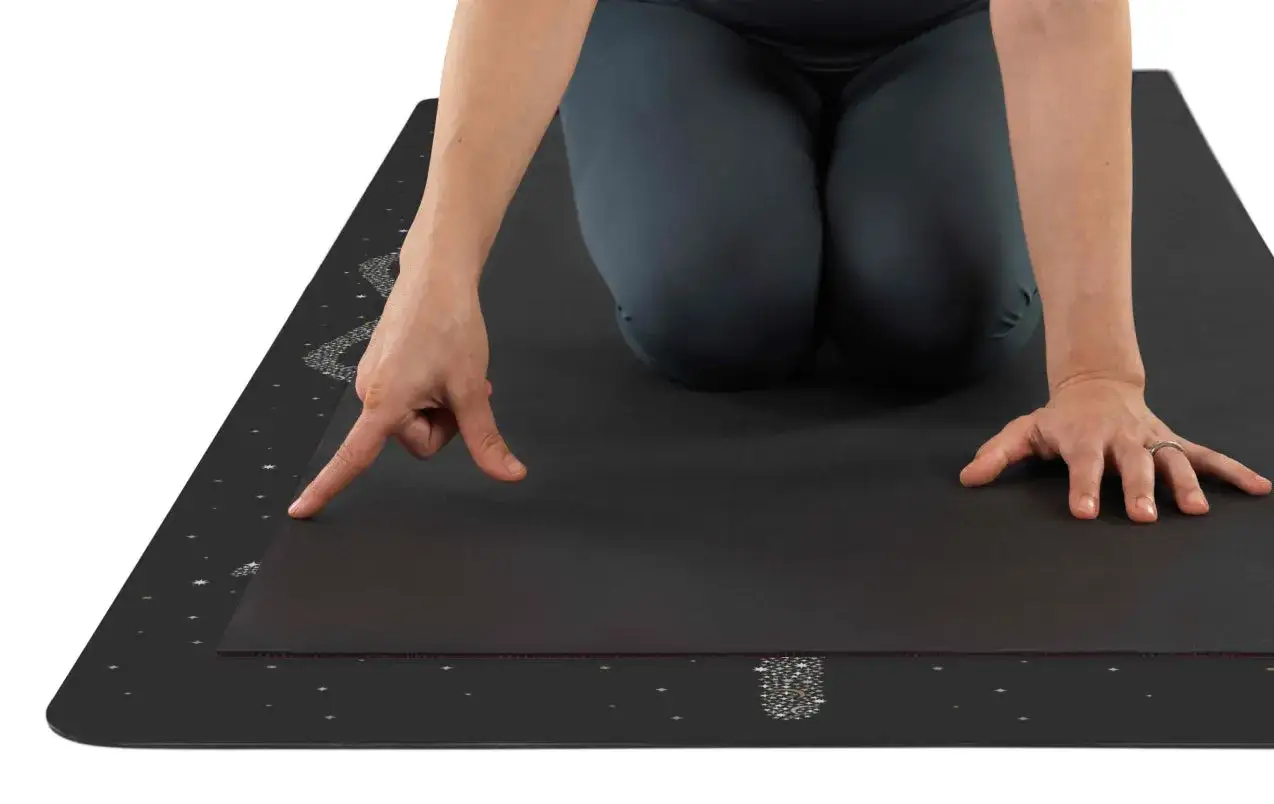 Une personne s'appr&ecirc;te &agrave; faire du yoga chez soi sur un tapis noir orn&eacute; d'&eacute;toiles.
