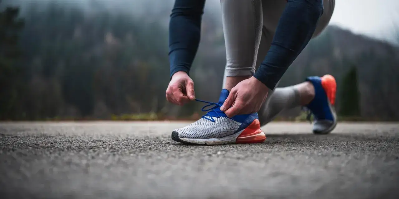 Biegacz sznuruje buty do biegania, przygotowując się do treningu w chłodny, mglisty dzień. Kluczowe jest, jak dobrać buty do biegania, by zapewnić komfort i bezpieczeństwo.