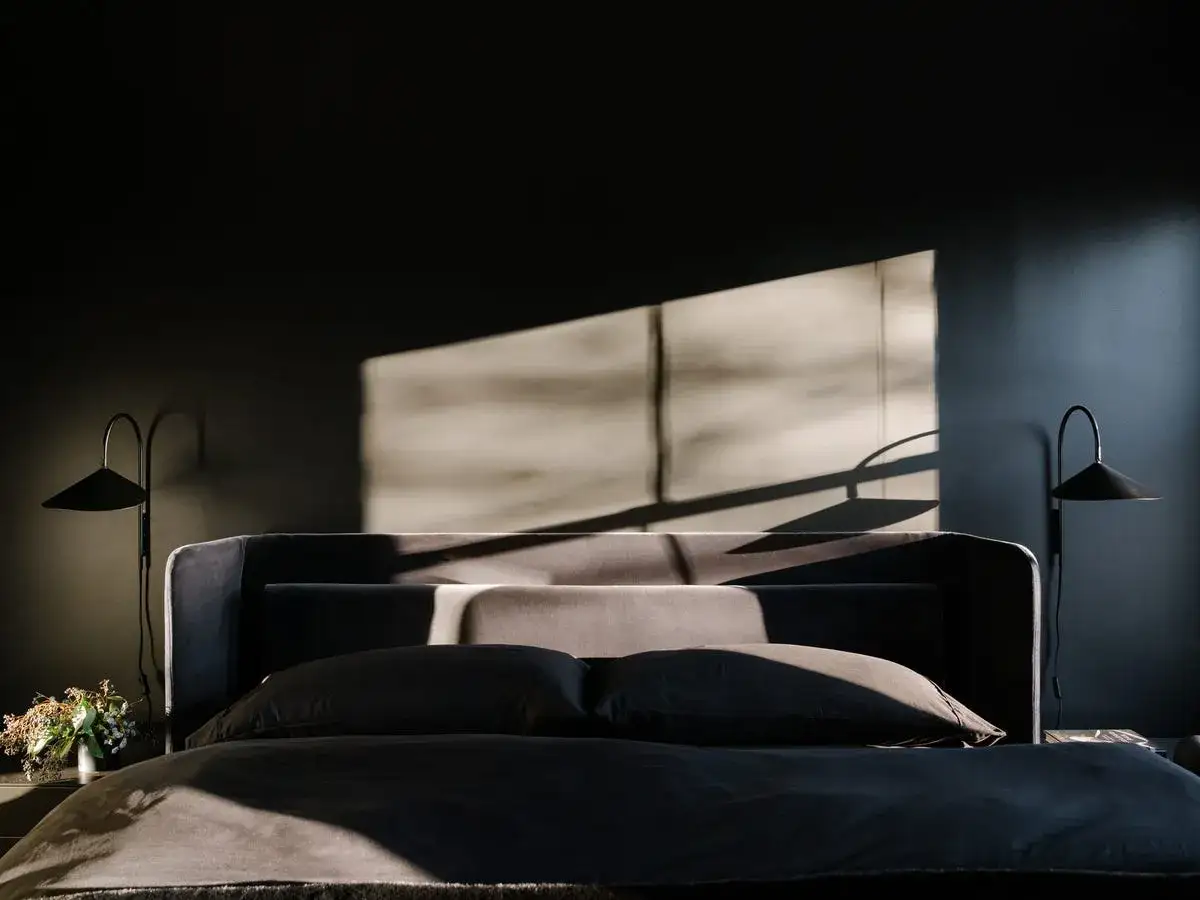 A dark, modern bedroom with a bed, two lamps, and a window shadow. It feels like waking up at 3am, with the light just starting to creep in.