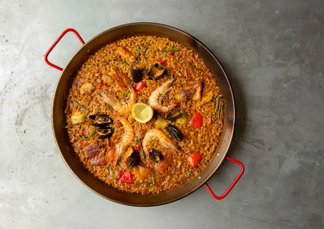 Pyszne hiszpańskie jedzenie: paella z owocami morza, ryżem, krewetkami, małżami i warzywami, ozdobiona cytryną.