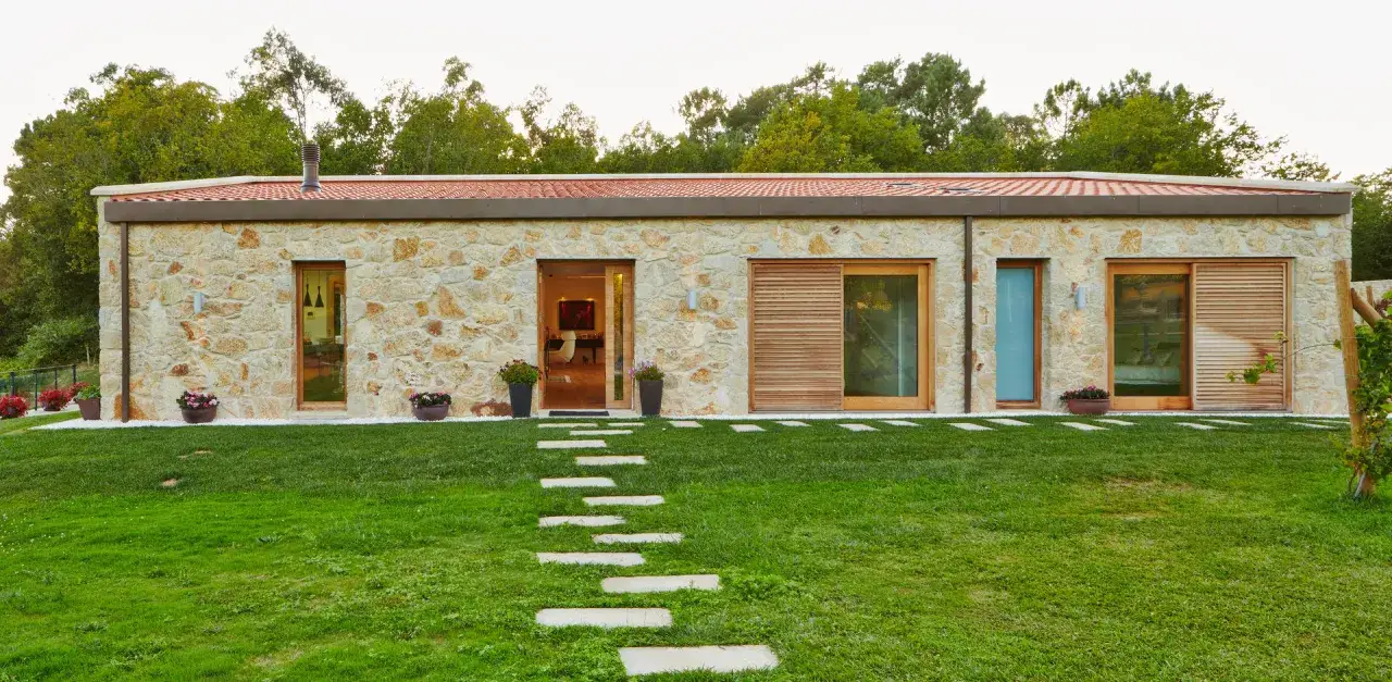 Casa unifamiliar de piedra con tejado rojo y camino de losas. Modernos modelos de casas unifamiliares integrados en la naturaleza.