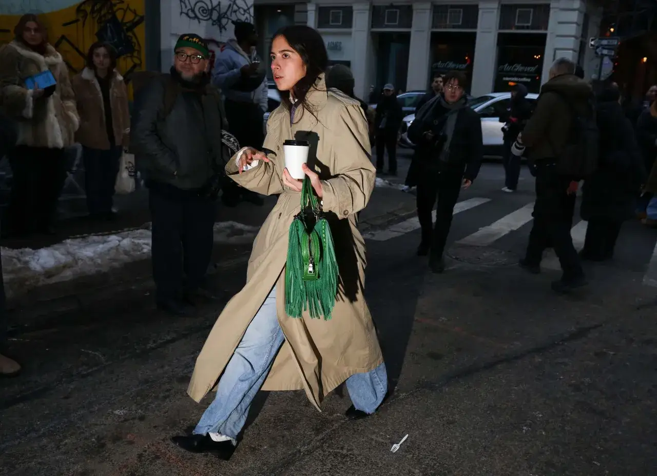 Kobieta w beżowym trenczu i jeansach, z zieloną torebką, idzie ulicą. Czarne, eleganckie buty to świetny wybór, jakie buty do trencza?