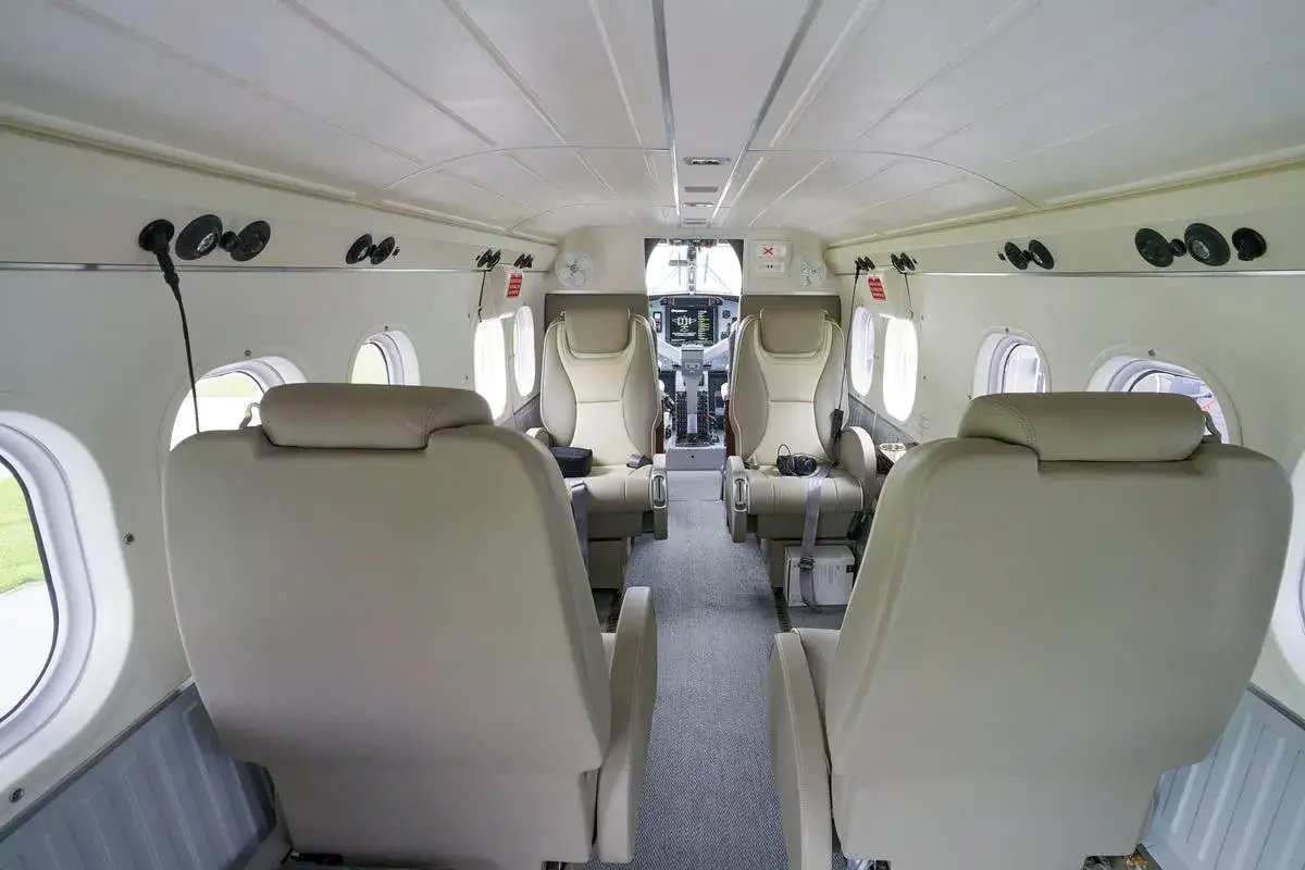 Innenraum eines Twin Otter Flugzeugs mit bequemen Sitzen und Blick auf das Cockpit.