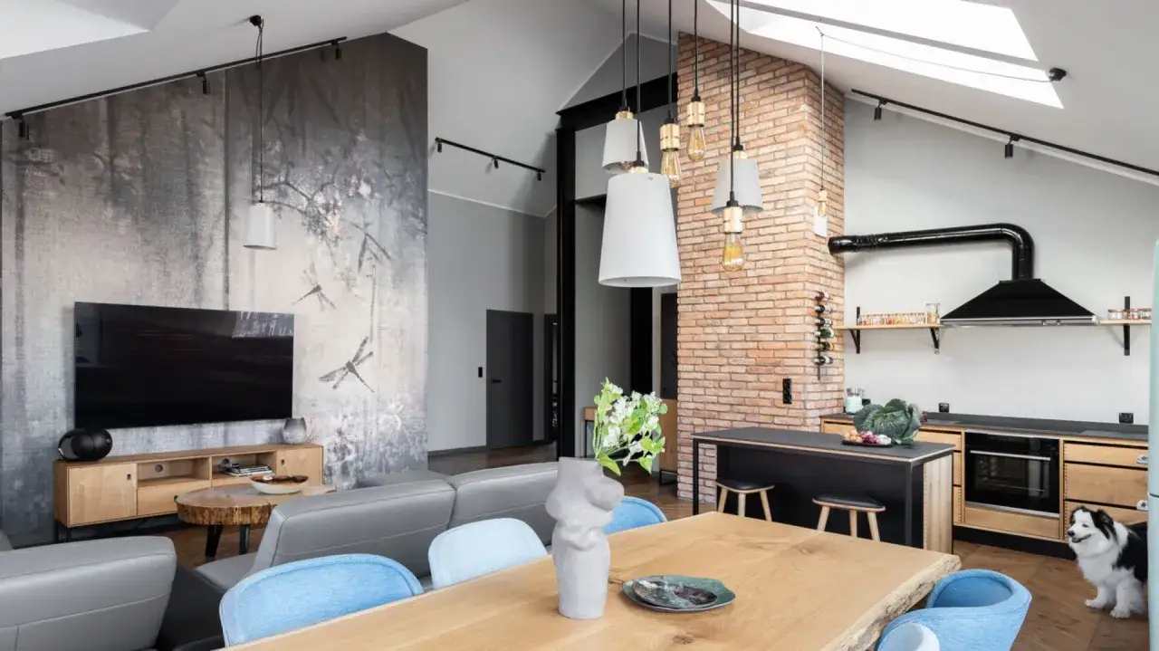 Salon loft inspiracje: szara sofa, drewniany st&oacute;ł, ceglana ściana i tapeta z ważkami tworzą przytulną przestrzeń.