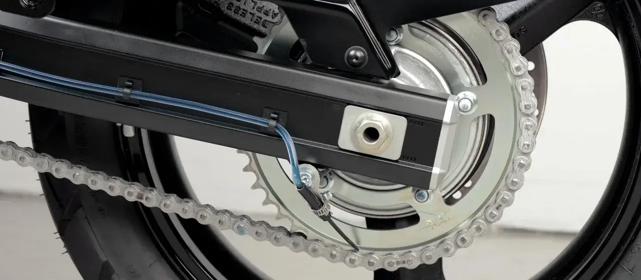 System automatycznego smarowania łańcucha w motocyklu, z niebieskim przewodem doprowadzającym olej do napędu.