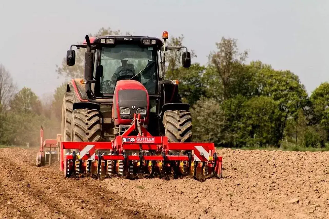 Czerwony traktor z agregatem uprawowym pracuje na polu. Kierowca z prawem jazdy kat T od ilu lat?
