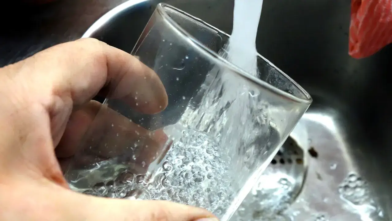 En hand håller ett glas som fylls med vatten från en kran. Bubblor syns i glaset, vilket kan tyda på klor i dricksvatten.