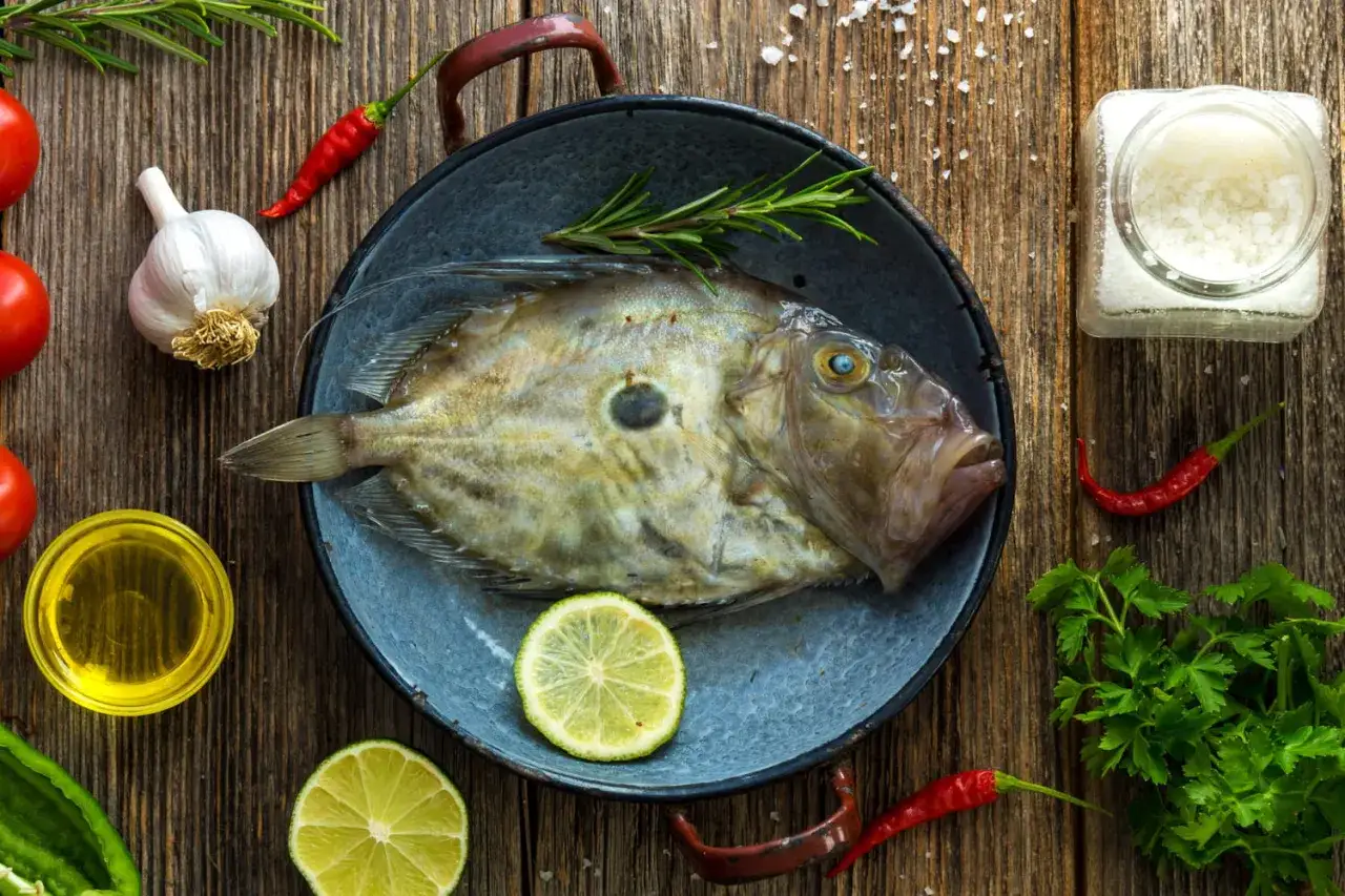 Un saint pierre frais, prêt à être cuisiné avec des herbes, des citrons, de l'ail et des piments sur fond de bois.