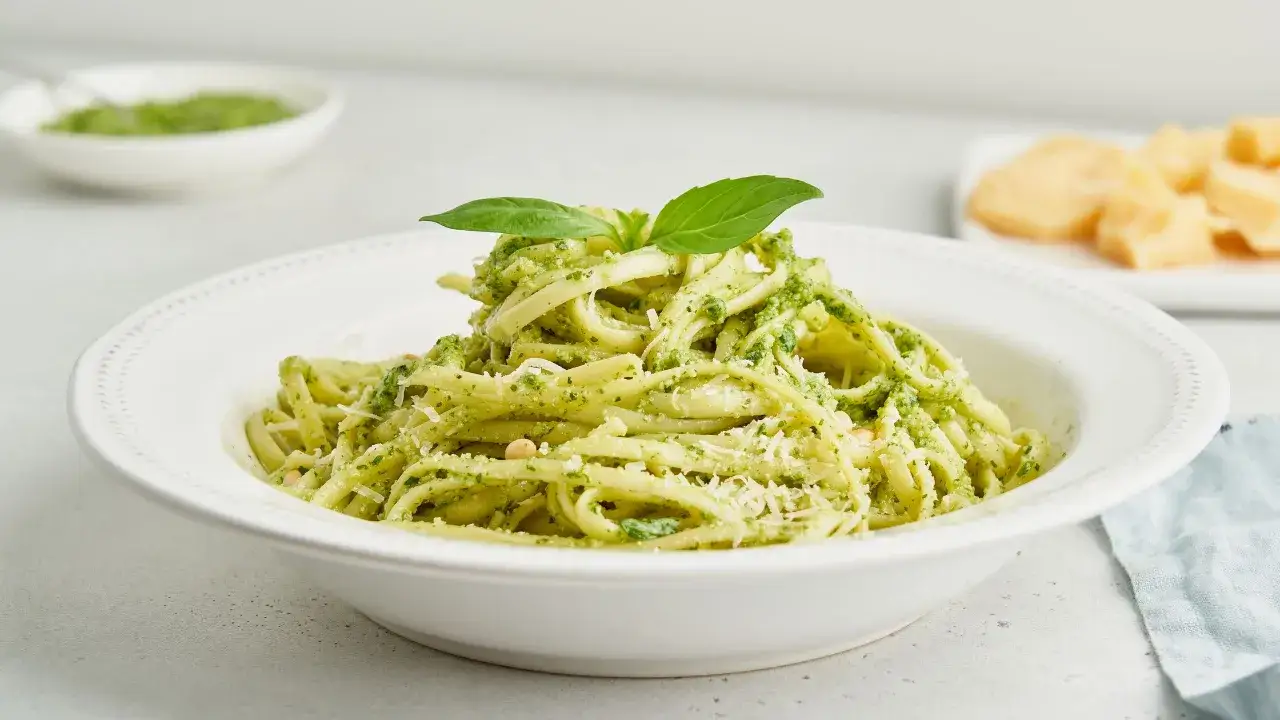 Linguine condite con un cremoso pesto di zucchine, guarnite con basilico fresco e parmigiano.