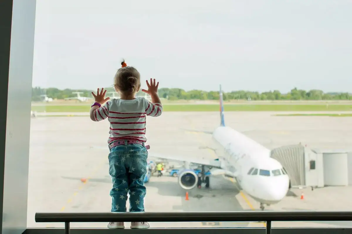 Litet barn med h&auml;nderna mot f&ouml;nstret, ser fram emot sitt flyg till K&ouml;penhamn. Ett flygplan st&aring;r redo vid gaten.