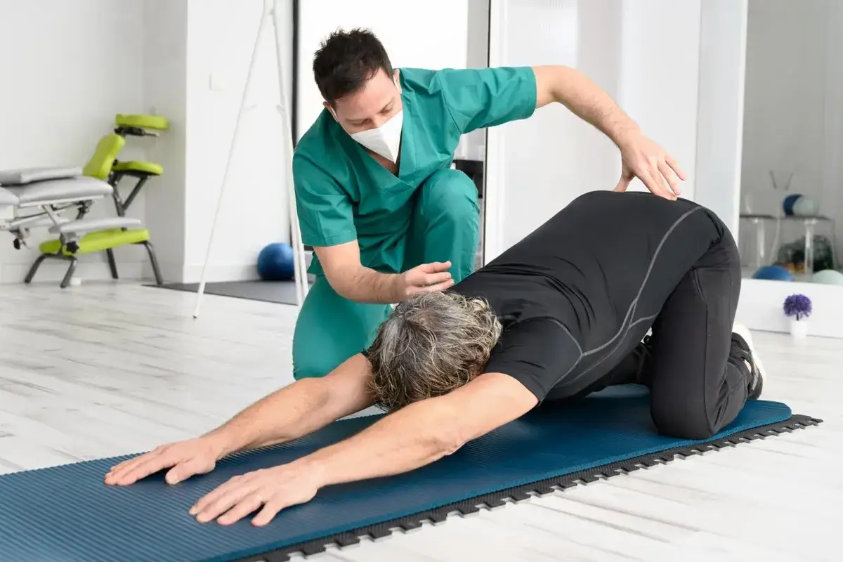 Un kin&eacute;sith&eacute;rapeute aide un patient &agrave; soulager son mal de dos avec un exercice. Un rem&egrave;de miracle pour le mal de dos.