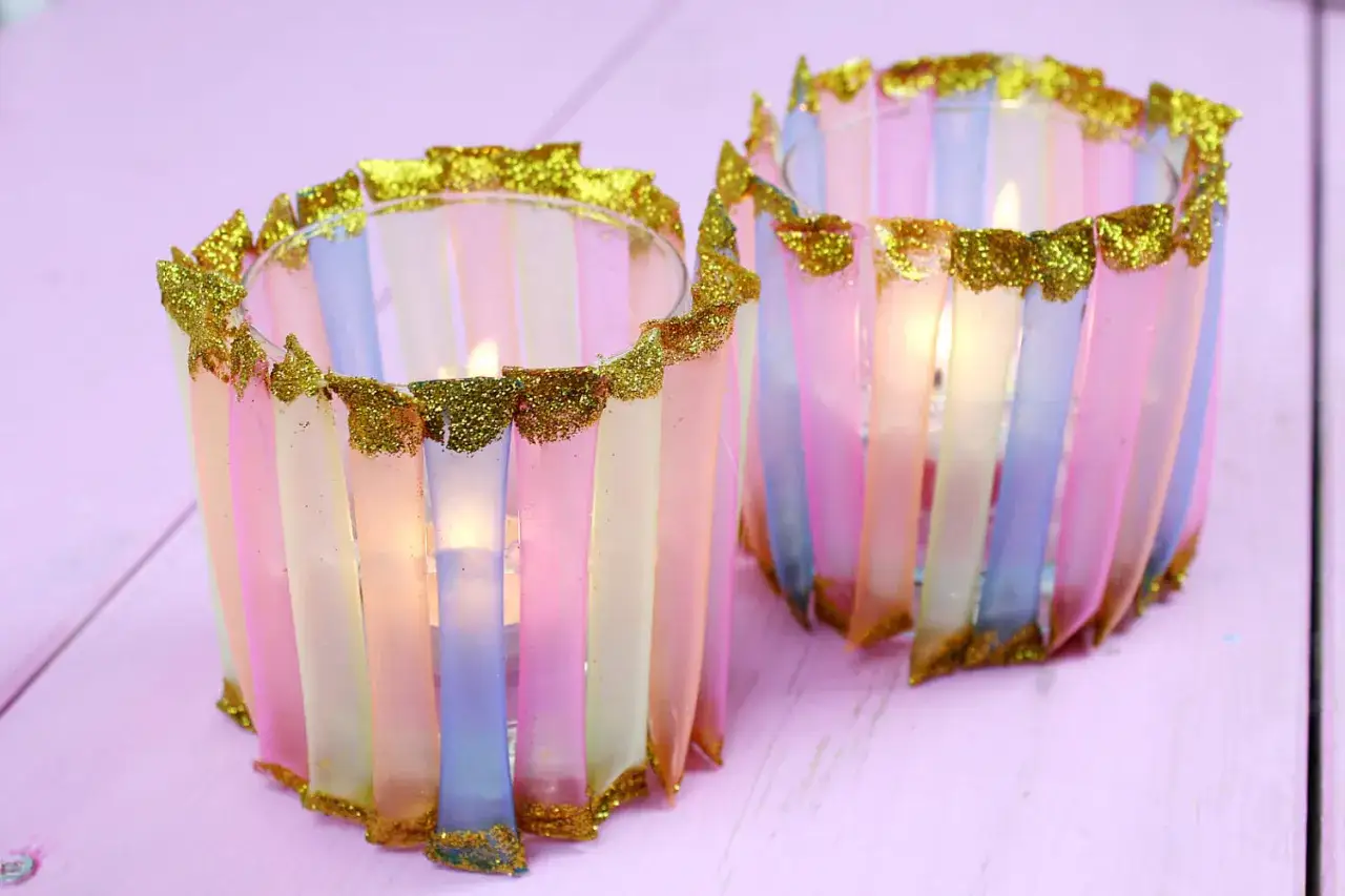 Zwei selbstgemachte Windlichter mit bunten Streifen und Goldglitzer. Ein schönes DIY-Projekt für gemütliche Abende.