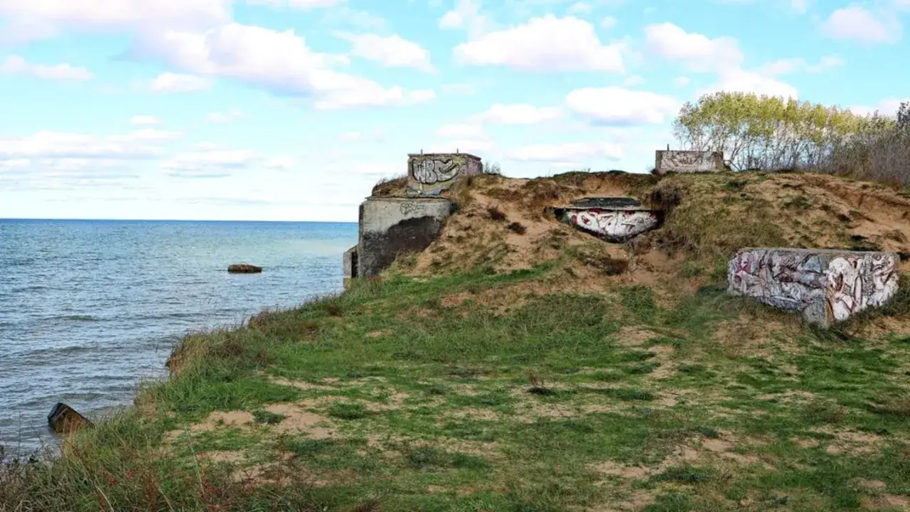 Verwitterter bunker am strand, mit Graffiti bemalt, thront auf einer sandigen Düne über dem Meer.