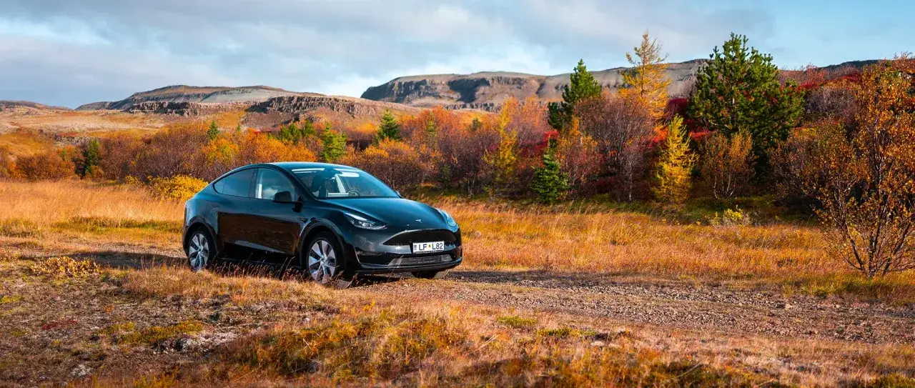 Schwarzer Tesla auf einer **Insel im September**. Herbstfarben leuchten in der Landschaft, Berge im Hintergrund.