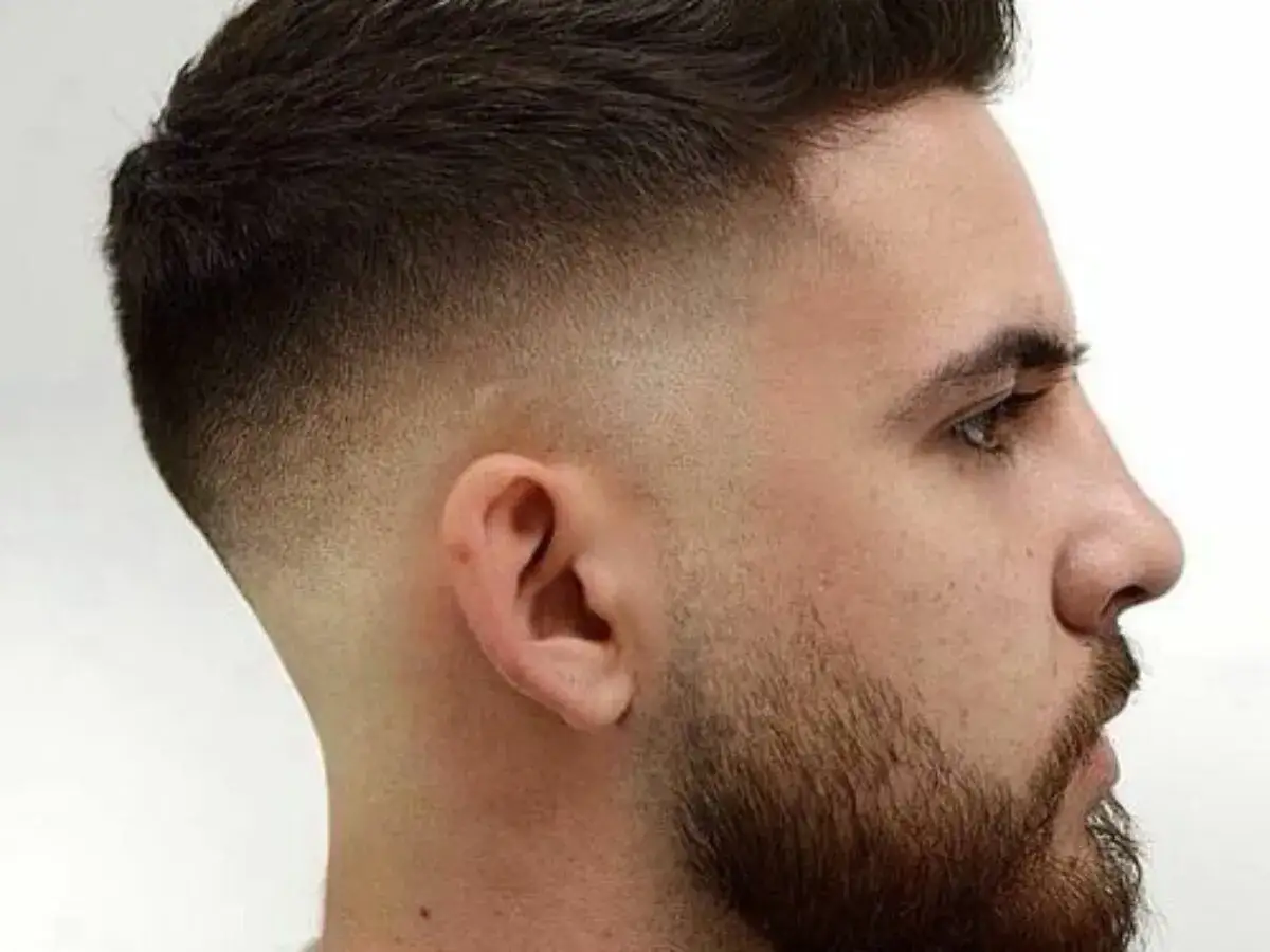 Un homme arbore une coupe de cheveux moderne avec un dégradé haut impeccable, mettant en valeur son style soigné.