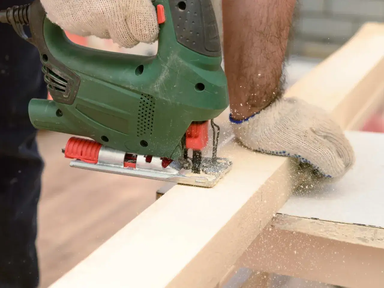 Main d'un bricoleur portant un gant utilise une scie toupie pour d&eacute;couper une planche de bois.