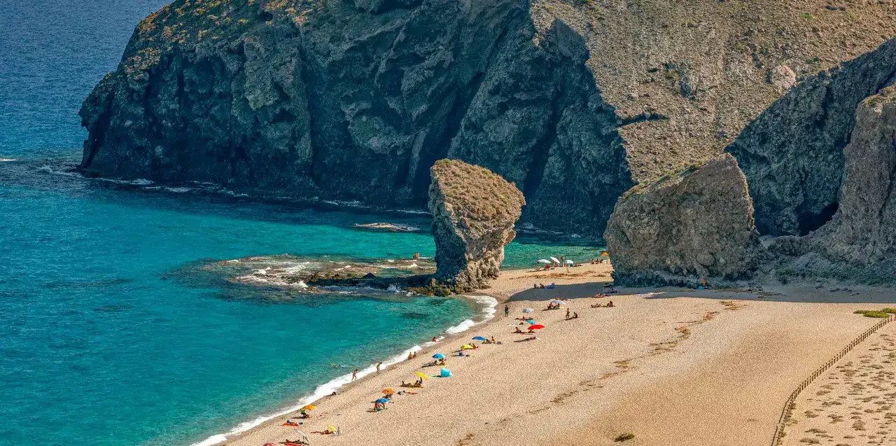 La playa de los Muertos, con sus aguas turquesas y formaciones rocosas imponentes, acoge a bañistas bajo sombrillas de colores.