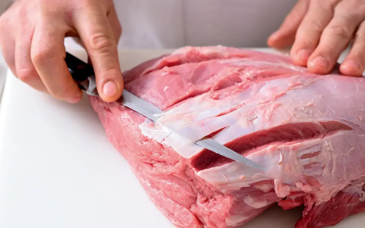 Mani esperte preparano un succulento arrosto di vitello, incidendo la carne per una cottura perfetta.