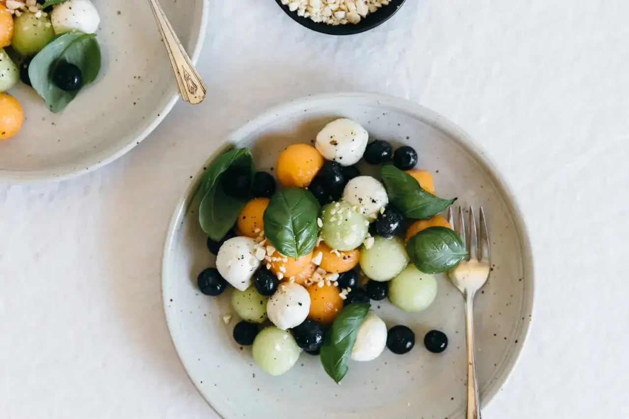 Erfrischender melonensalat mit mozzarella, Blaubeeren und Basilikum, garniert mit gehackten N&uuml;ssen.