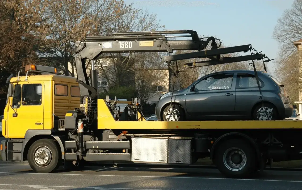 Gelber Abschleppwagen mit Kran hebt graues Auto auf Ladefläche. Der Abschleppdienst wurde gerufen, da das Auto vorher weggefahren war.