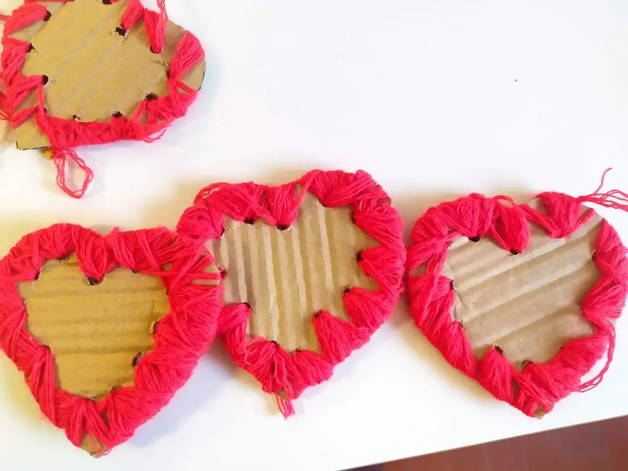 Tre cuori di cartone decorati con lana rossa, un simpatico modellino cuore fai da te.