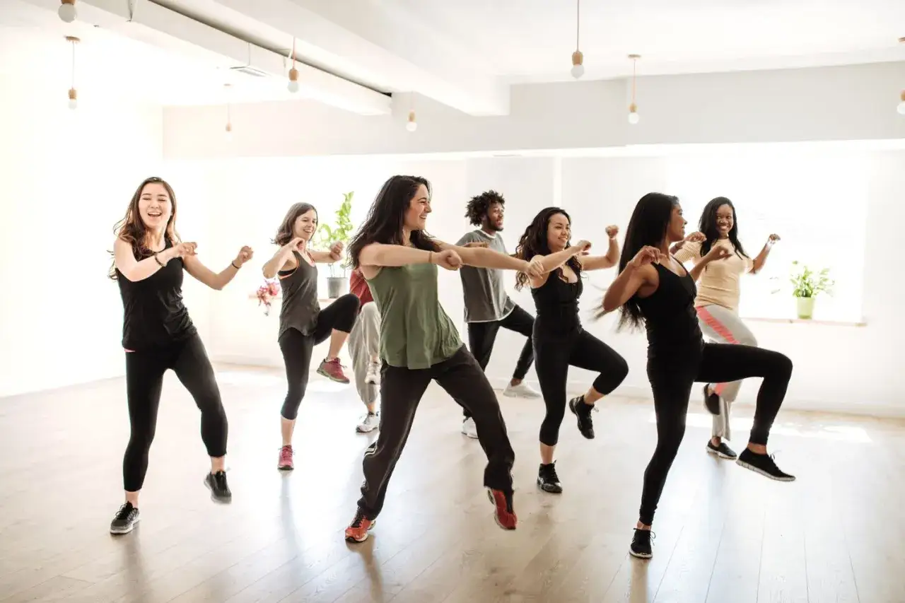 Grupa ludzi tańczy wesoło, wykonując energiczne ruchy. To właśnie zumba – świetna zabawa i trening w jednym!