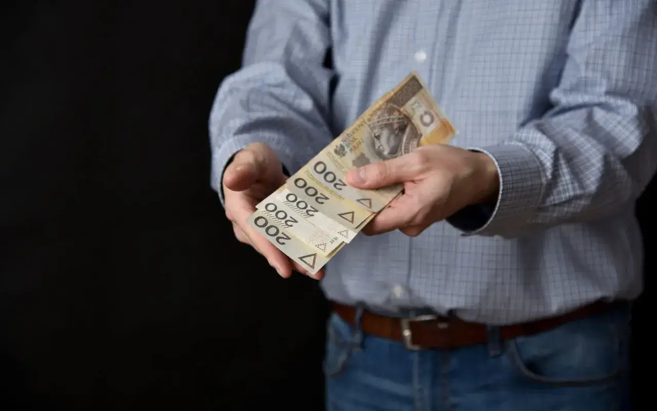Ręce trzymające banknoty 200 zł. Może to symbolizować spłatę zobowiązań lub sprzedaż długów.