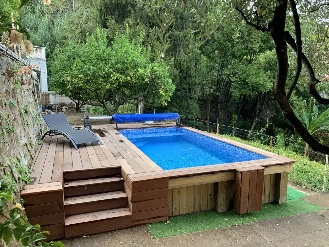 Petit jardin am&eacute;nag&eacute; autour d'une piscine hors sol avec terrasse en bois et transat. Un coin d&eacute;tente parfait.