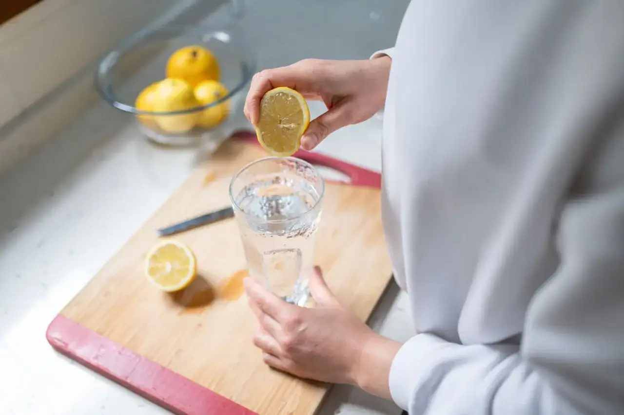 Una persona exprime un lim&oacute;n en un vaso de agua. El agua con lim&oacute;n es buena para la digesti&oacute;n y la hidrataci&oacute;n.