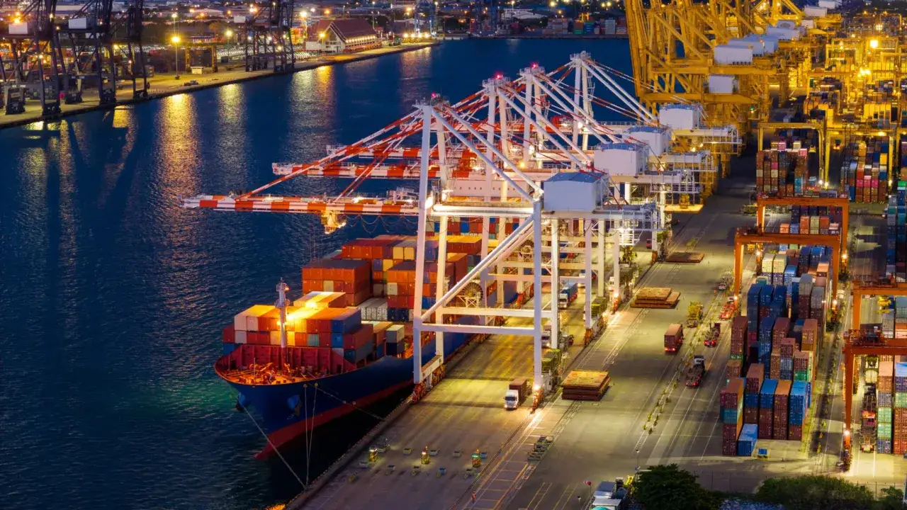 Ein Frachtschiff wird im Hafen von Kr&auml;nen beladen. Container stapeln sich auf dem Schiff und am Kai, bereit f&uuml;r den Transport.