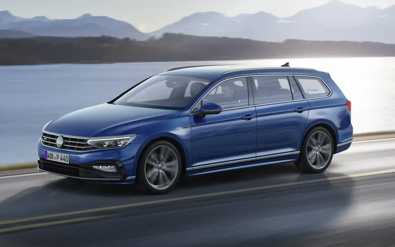 Niebieski Volkswagen Passat Variant, reprezentant segmentu kombi, przemierza malowniczą trasę nad jeziorem.