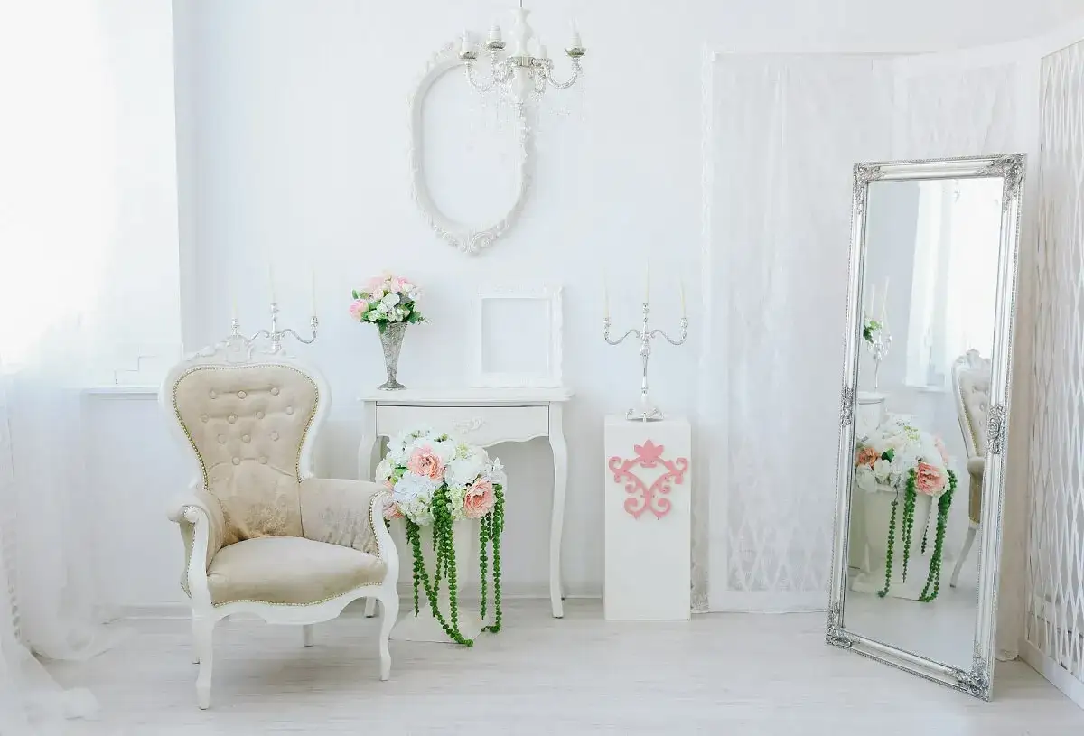 Elegancki salon w stylu shabby chic. Jasna, przestronna aranżacja z fotelem, lustrem, świecznikami i bukietami kwiatów.
