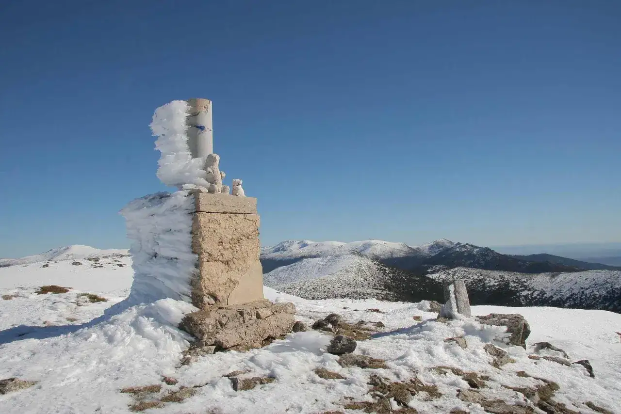 Piedra cubierta de hielo en la cima de una montaña con forma de mujer, con picos nevados al fondo.