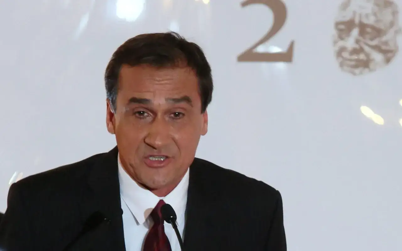 Mariusz Max Kolonko w garniturze, mówiący do mikrofonu. W tle cyfra 2 i portret.