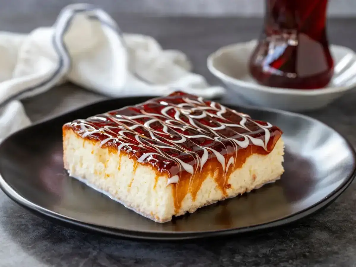 Una fetta di torta trilece ricetta, bagnata da una glassa caramellata e decorata con fili bianchi, su un piatto nero.