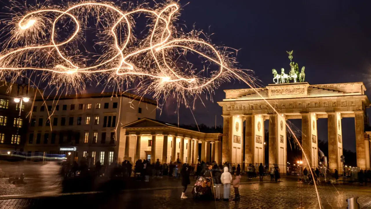 Silvester am Brandenburger Tor: Funken spr&uuml;hen in der Nacht und malen die Jahreszahl 2020 in den Himmel. Menschen versammeln sich, um das neue Jahr zu begr&uuml;&szlig;en.